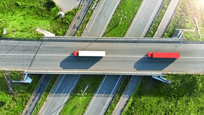 Truck Logistics Aerial. Two Trucks Motion By The Highway Intersection Road Between Fields. View From Drone.