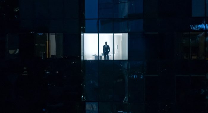 Aerial Shot: From Outside Into Office Building With Businessman Looking Out Of The Window. Beautiful Shot Of The Financial Business District Skyscrapers In The Evening.